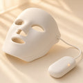 Halo Glow LED face mask, corded to its handheld controller, on a seamless cream backdrop in warm window light