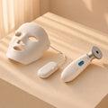 The Clear Glow Set: LED face mask with corded controller and pore wand on a cream plaster plinth